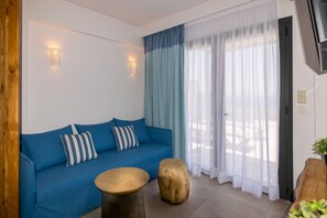 A room with a blue sofa, two wooden stools, a small round table, and a large window with sheer curtains. - Varkotopi villa 1,Pool,Near the Beach,South Crete (Rethymno)