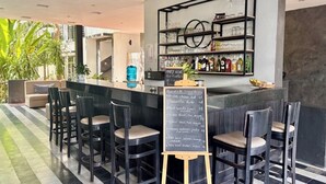 Zona de bar con una pizarra de menú, taburetes y estantes llenos de copas y botellas.