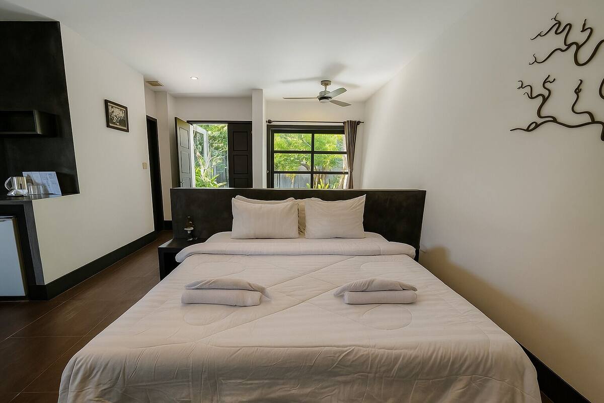 A hotel room with a large bed, a desk with a chair, a window with curtains, and a ceiling fan.