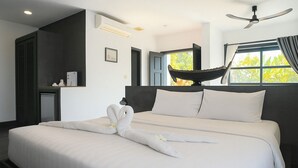 Una habitación de hotel moderna con una cama grande, un ventilador de techo y una ventana con vista a árboles.