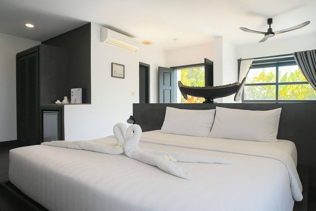 A modern hotel room with a large bed, a ceiling fan, and a window with a view of trees.