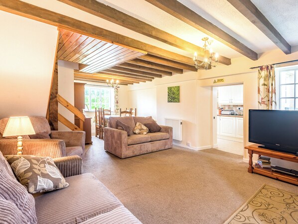 A living room with a sofa, chairs, a TV, and a wooden ceiling structure.