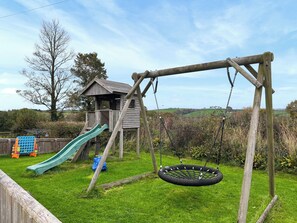 A wooden play structure with a slide and swing set in a grassy yard.