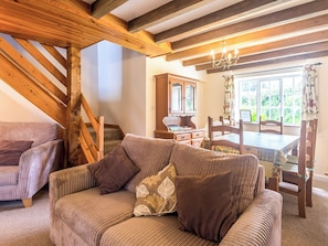 A cozy room with a wooden staircase, a sofa with cushions, a wooden dining table, and a window with curtains. - Well Farm Cottage - UK11879 (Holsworthy, near Launceston)