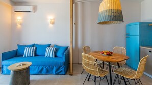 Una sala de estar moderna con un sofá azul, sillas de mimbre, una mesa de comedor de madera con fruta y un refrigerador azul.