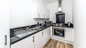 Eine moderne Küche mit weißen Schränken, einer schwarzen Arbeitsplatte, einer Edelstahl-Dunstabzugshaube, einer Mikrowelle und einem Backofen.