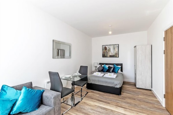 Una habitación de hotel moderna con cama, escritorio con sillas, sofá, espejo y un cuadro en la pared.