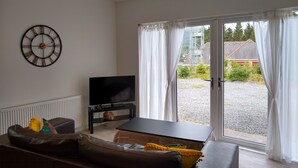 Una sala de estar con televisor de pantalla plana, sofá, mesa de centro y un amplio ventanal con cortinas.