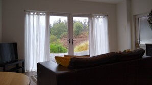 Una sala de estar con un sofá, un televisor y un ventanal corredera que da a un jardín.
