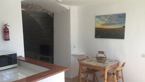 A kitchen with a microwave, a stone fireplace, a dining table with chairs, and a painting on the wall.