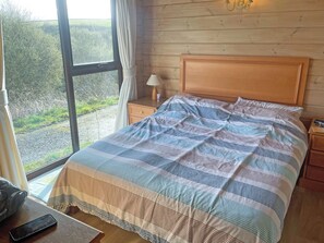 A bed with a striped bedspread, a wooden headboard, a bedside lamp, and a view of greenery outside.