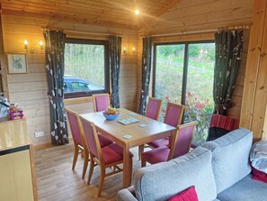 L’intérieur d’un chalet en bois comprend une table à manger, des chaises, un canapé et de grandes fenêtres avec des rideaux.