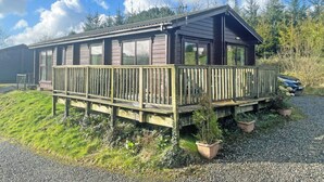 A wooden cabin with a deck, large windows, and a gravel driveway.