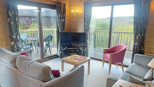A furnished room with a sofa, armchairs, a table, a TV, and a balcony with a view.