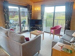 A furnished room with a sofa, armchairs, a table, a TV, and a balcony with a view.