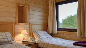 A room with two beds, a nightstand, a lamp, and a window with curtains.