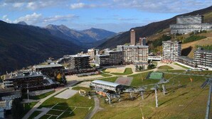 A modern hotel complex with multiple buildings, a central courtyard, and a mountainous backdrop. - Studio for 2 at slopes, pets allowed (Les Menuires)