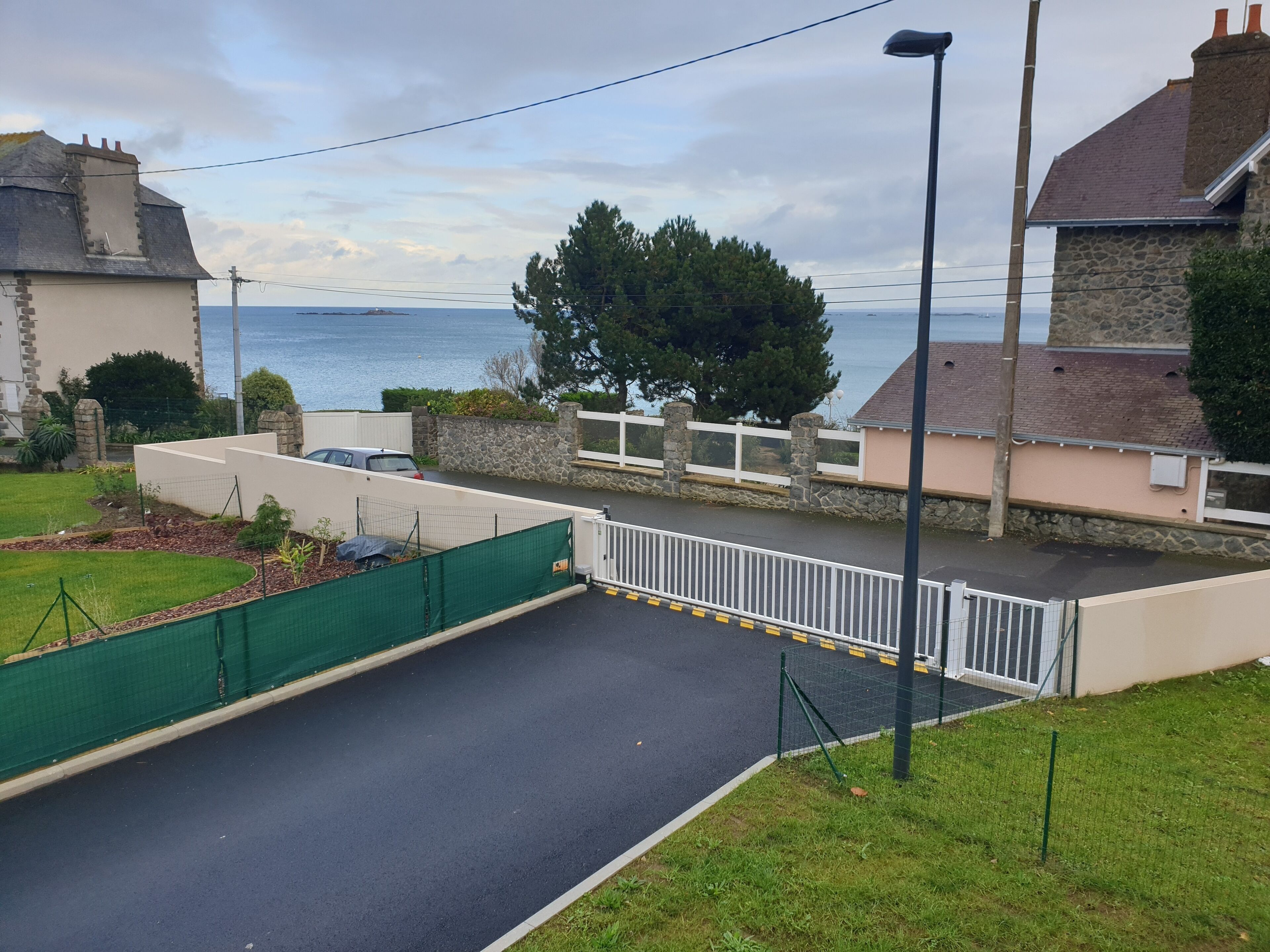 A residential street with a paved driveway, a white fence, and a stone wall.