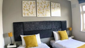 Habitación de hotel con dos camas, un cabecero oscuro y tres cuadros florales.