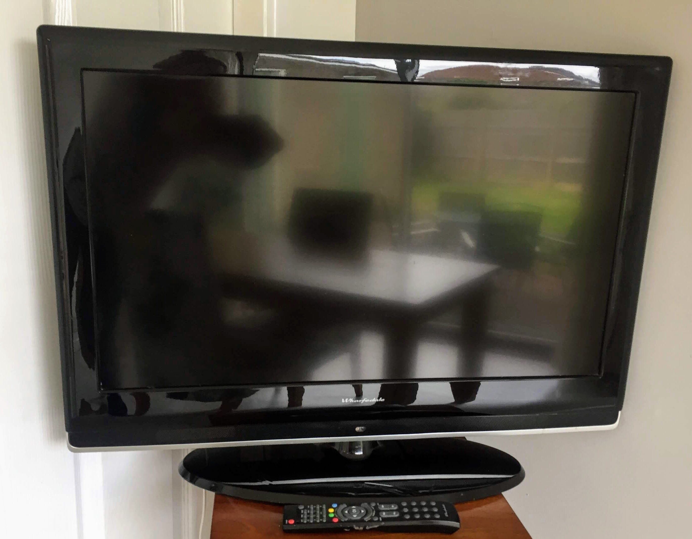 Un téléviseur à écran plat fixé au mur, avec une télécommande posée sur un petit meuble en bois situé en dessous.