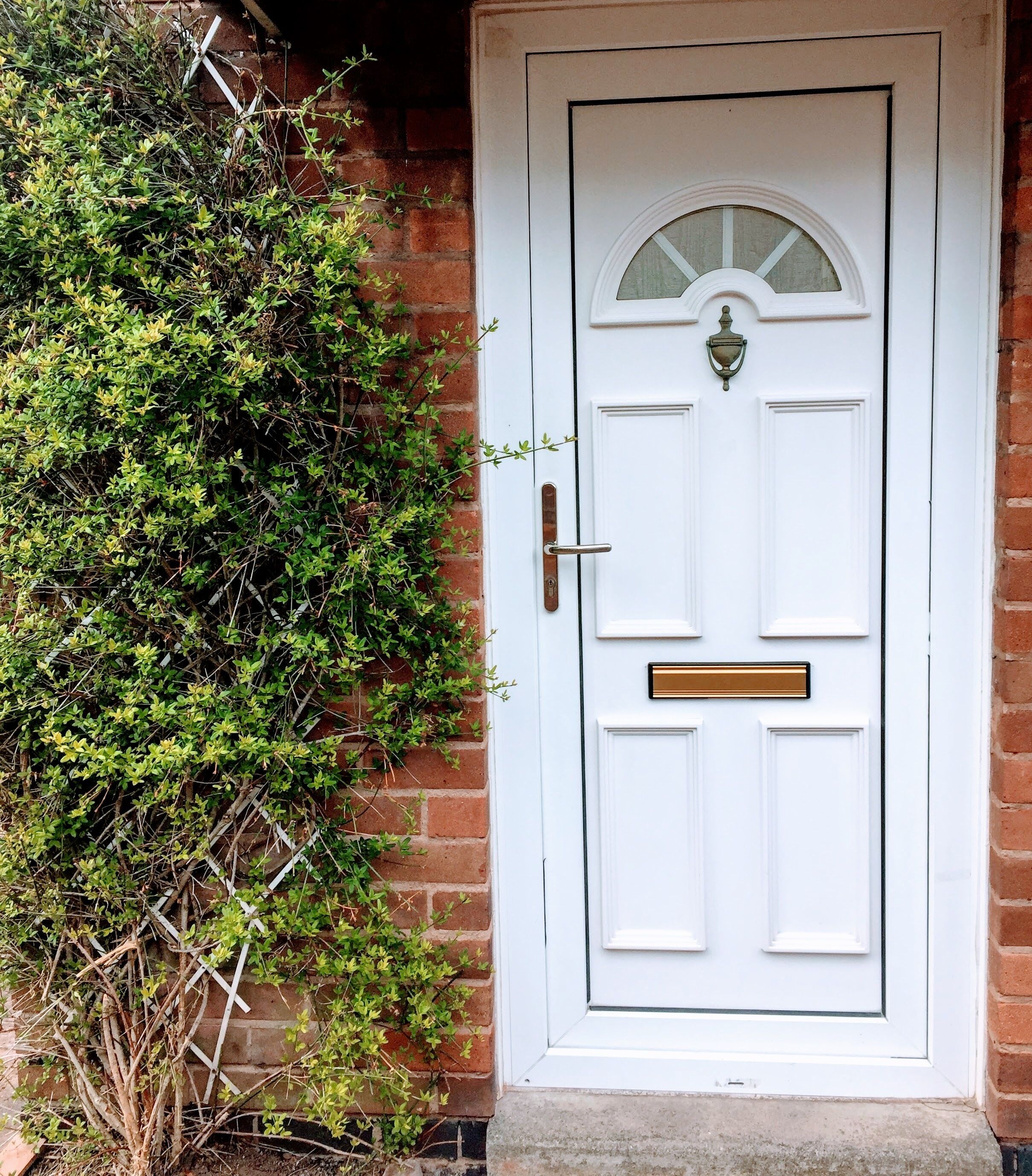A white front door with a brass knocker, a mail slot, and a small window above the door.