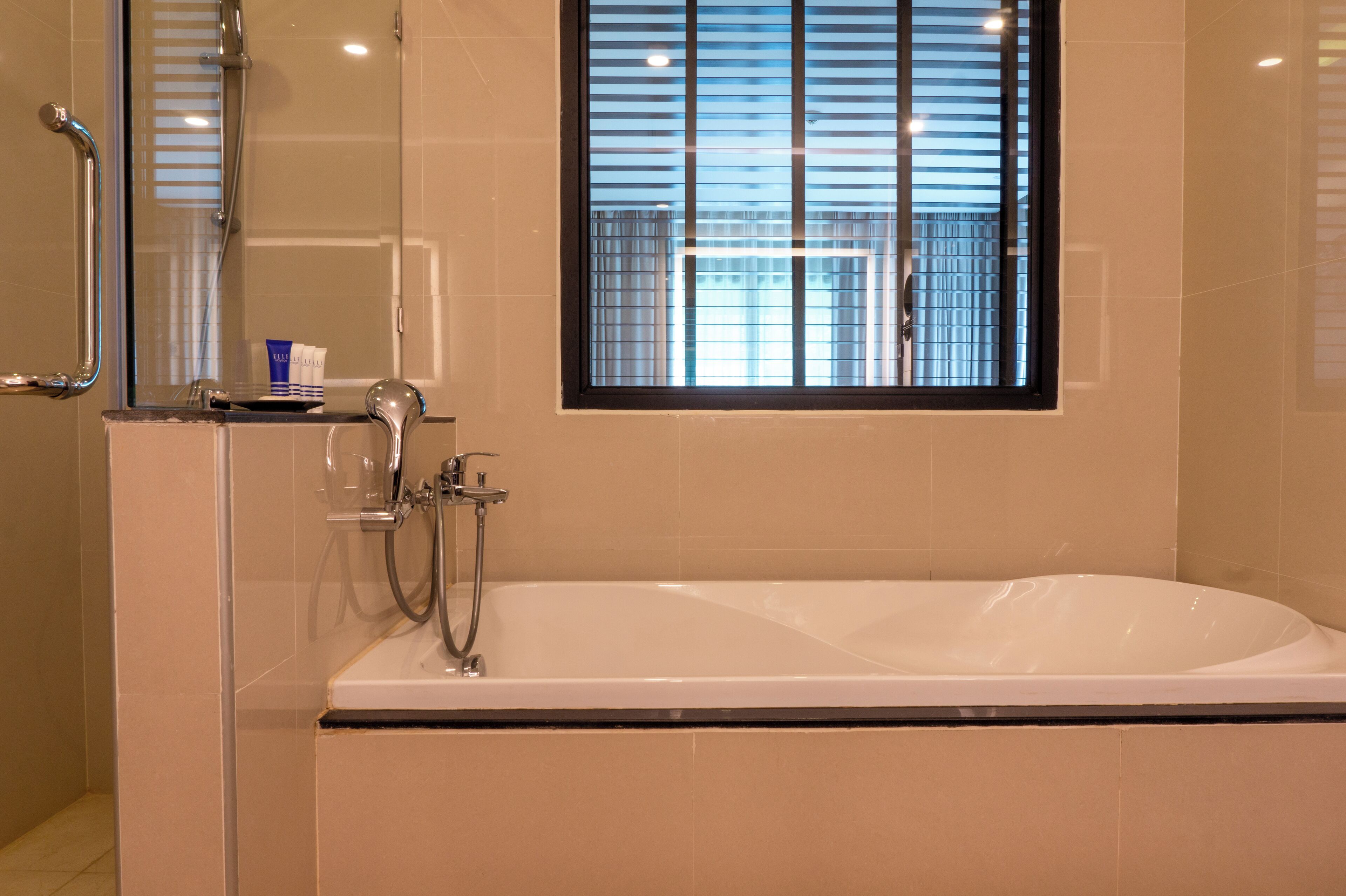 Un baño moderno con bañera, cabina de ducha de cristal y ventana con persianas.