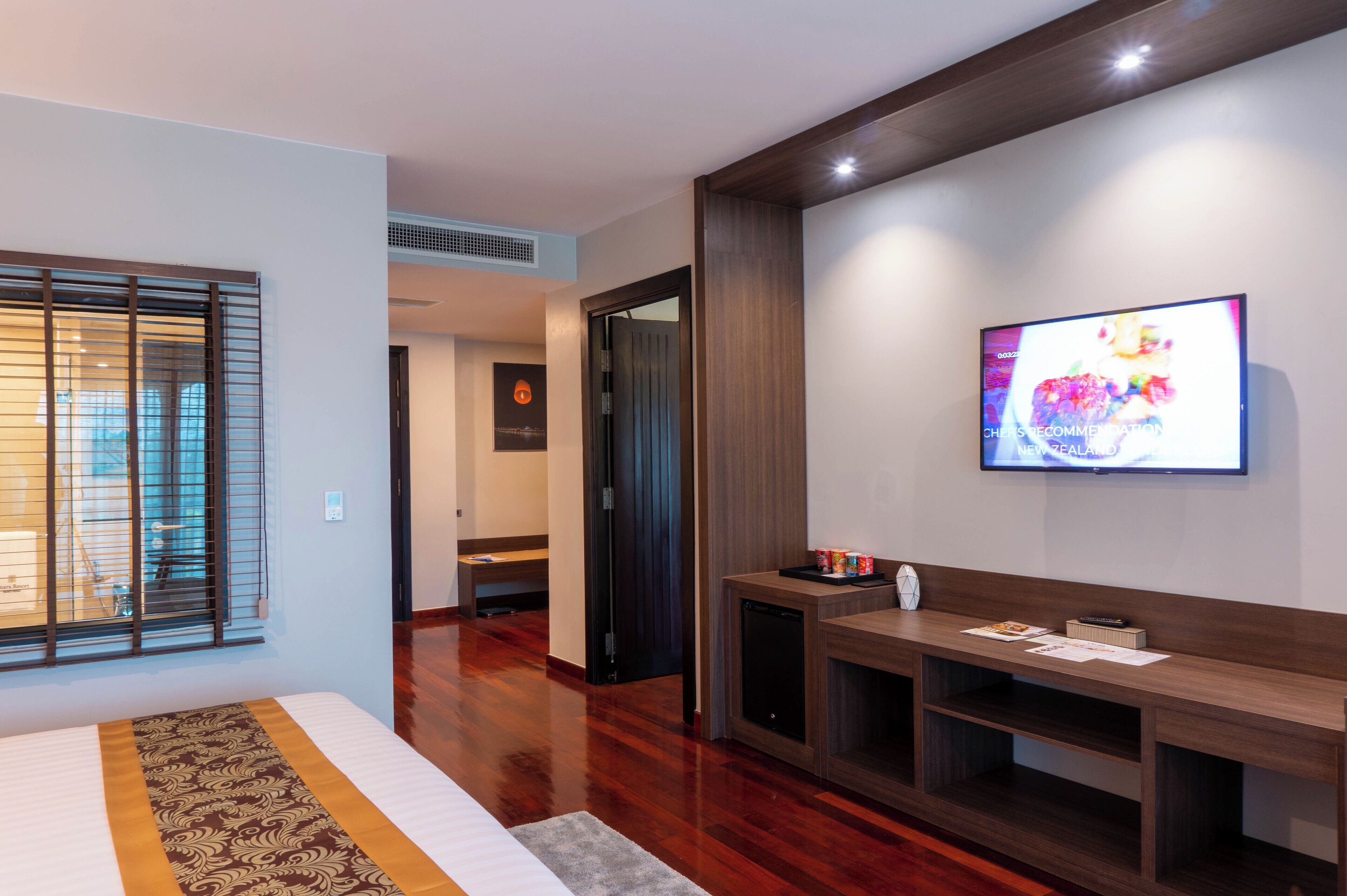 Ein modernes Hotelzimmer mit einem großen Bett, einem an der Wand montierten Fernseher, einer Holzbank und einem kleinen Tisch mit Fernbedienung.