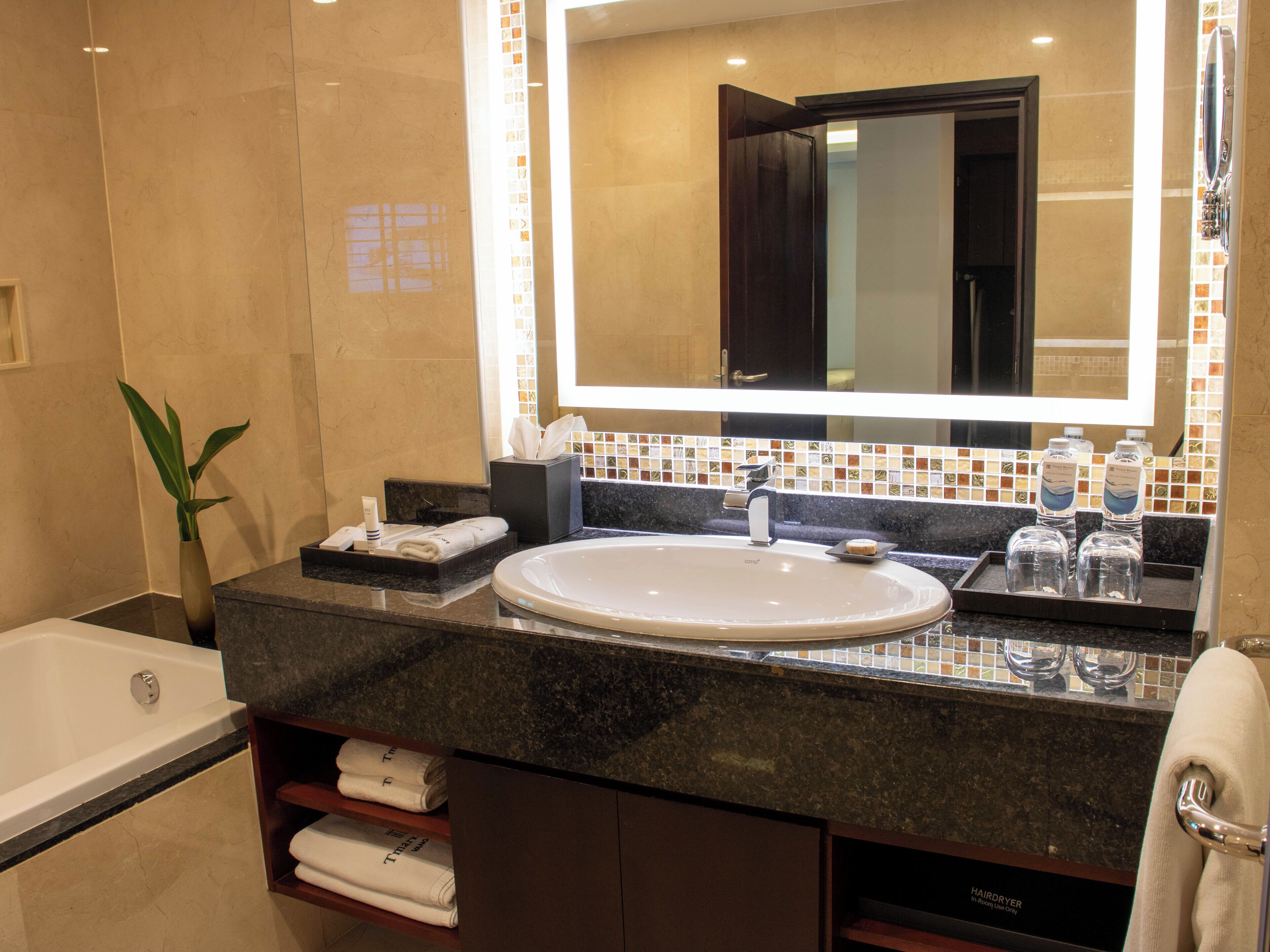 A modern bathroom with a large sink, a mirror, and a bathtub. There are towels and toiletries on the counter.