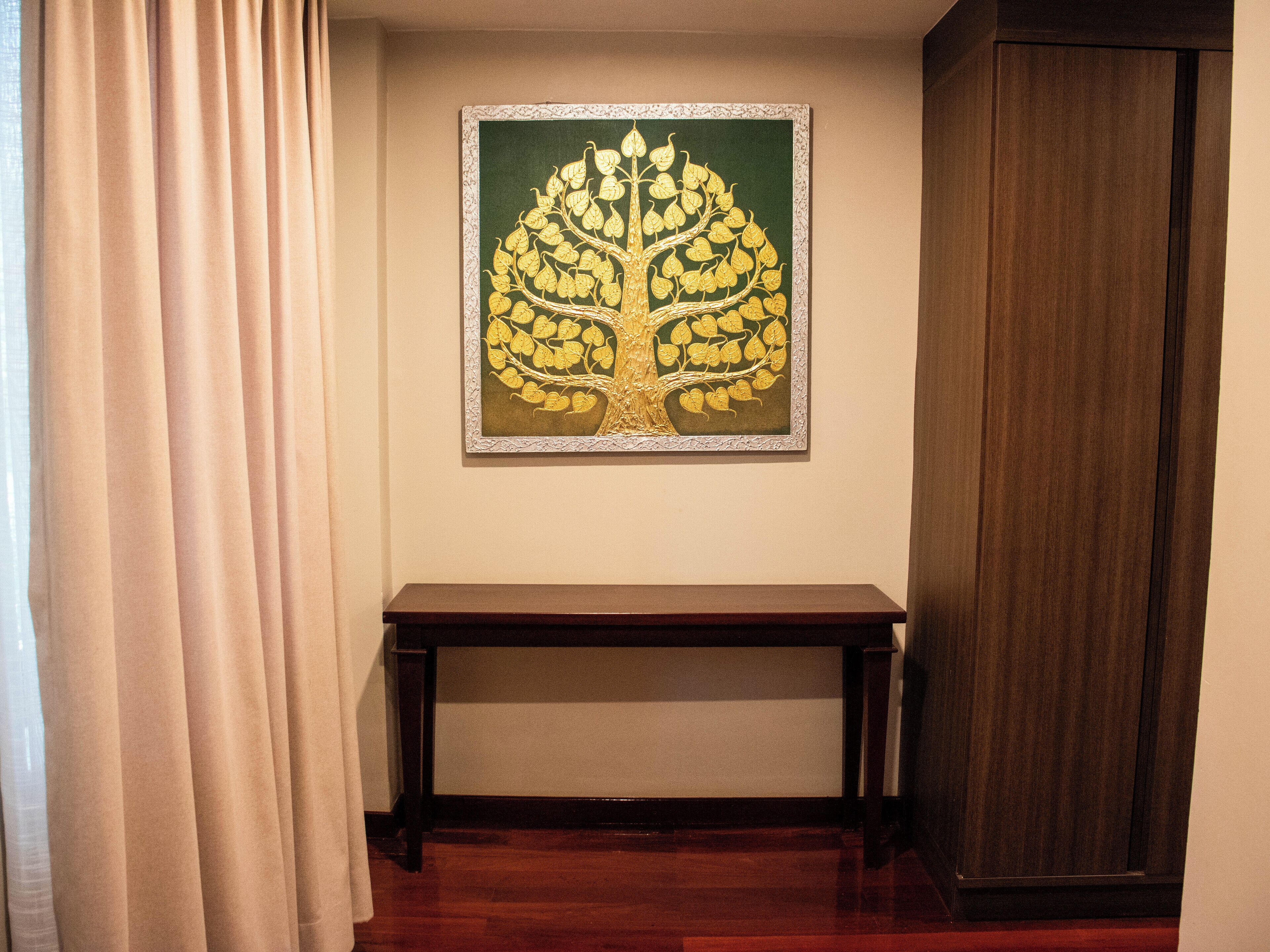 A room with a wooden bench, a framed artwork of a tree on the wall, and a wooden door.