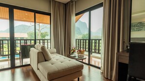 A modern hotel room with a large sofa, a small table with a vase and fruit basket, and a balcony with a view of mountains. - Tmark Resort Vang Vieng (Vang Vieng)