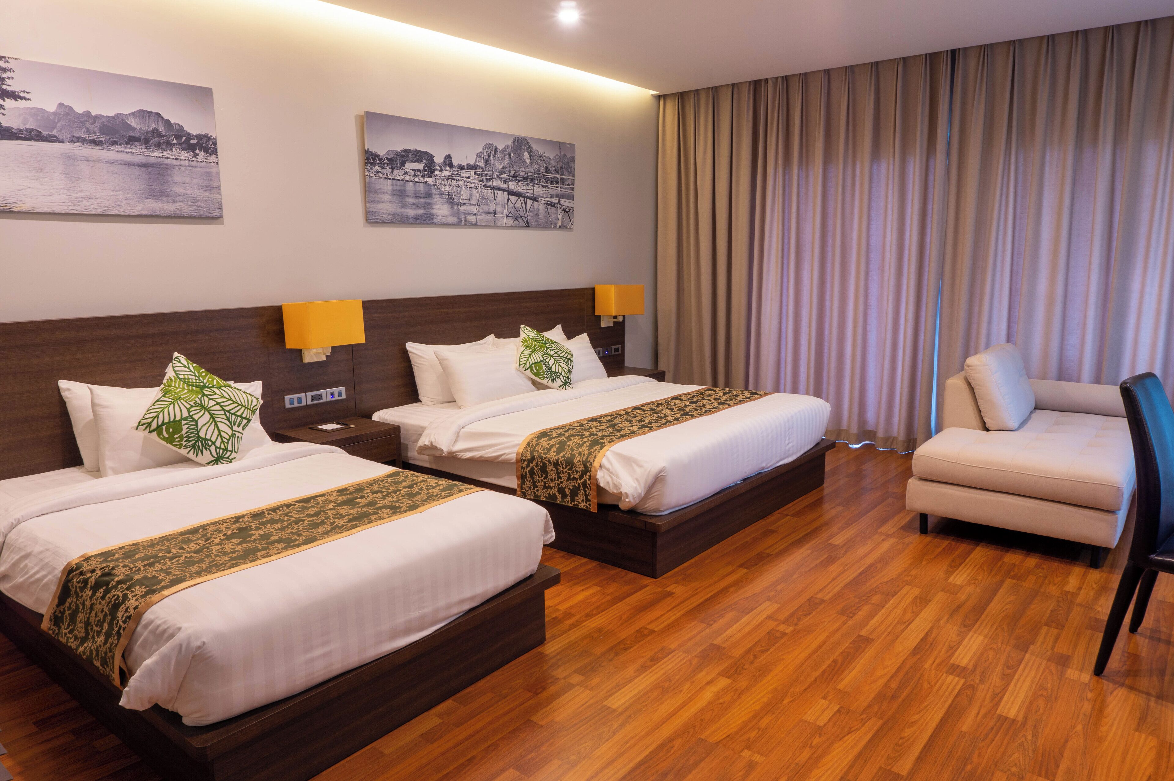 A hotel room with two beds, a sofa, and a chair. There are two wall-mounted lamps and two paintings.