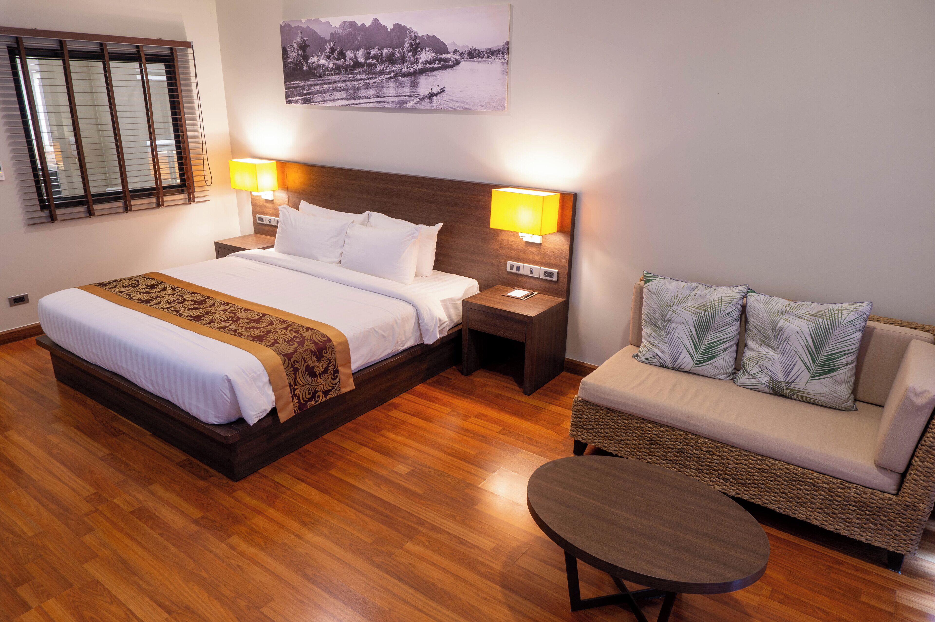 Una habitación de hotel con una cama grande, un sofá, una mesita y dos lámparas de noche.