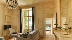 Amplia sala de estar con sofá, sillón y televisión. Hay una ventana con cortinas, una chimenea y un espejo.