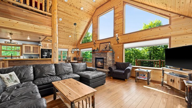 A spacious living area with a fireplace, wooden flooring, and large windows offering a view of the outdoors.