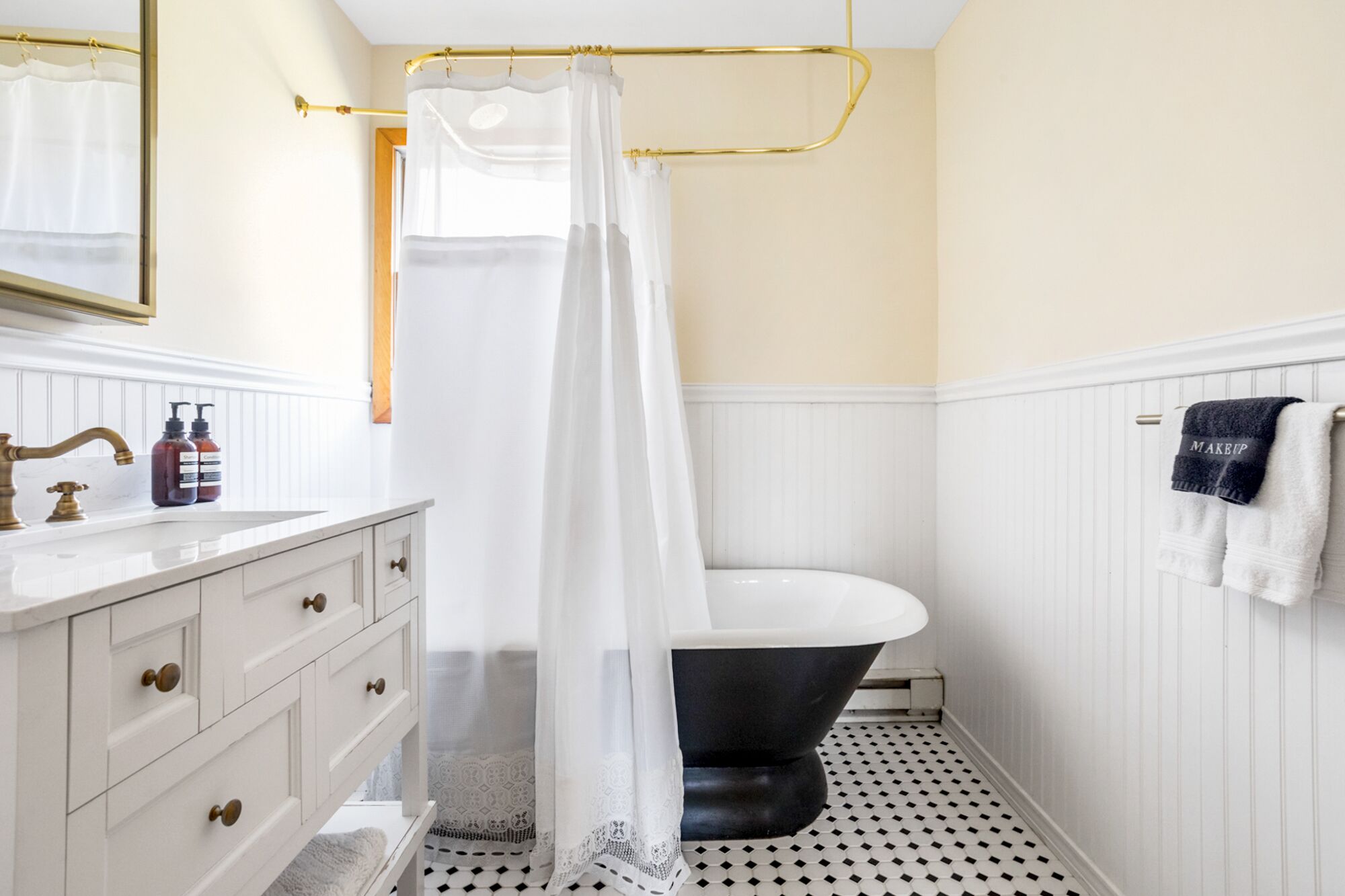 A bathroom with a white vanity, a black bathtub, and a gold shower curtain rod.