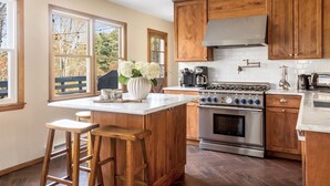 A kitchen with wooden cabinets, a stainless steel stove, and a large window with a view of trees.
