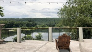 A wooden deck with a view of a lake and forest, a wooden chair, and string lights.