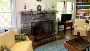 Ein gemütliches Wohnzimmer mit Kamin aus Stein, bequemen Sitzmöglichkeiten, einem Fernseher und einer Bücherwand voller Bücher.