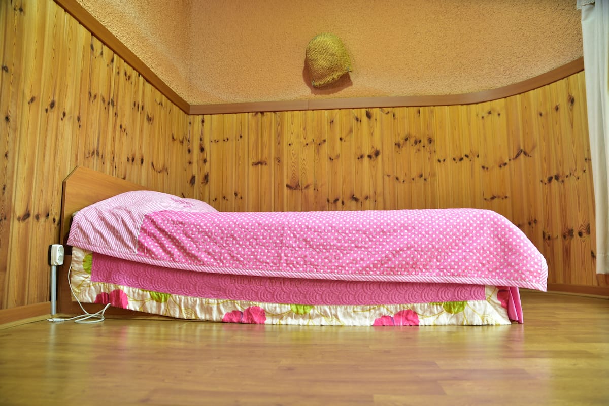 Ein Einzelbett in einem Raum mit Holzwandverkleidung und Holzboden.
