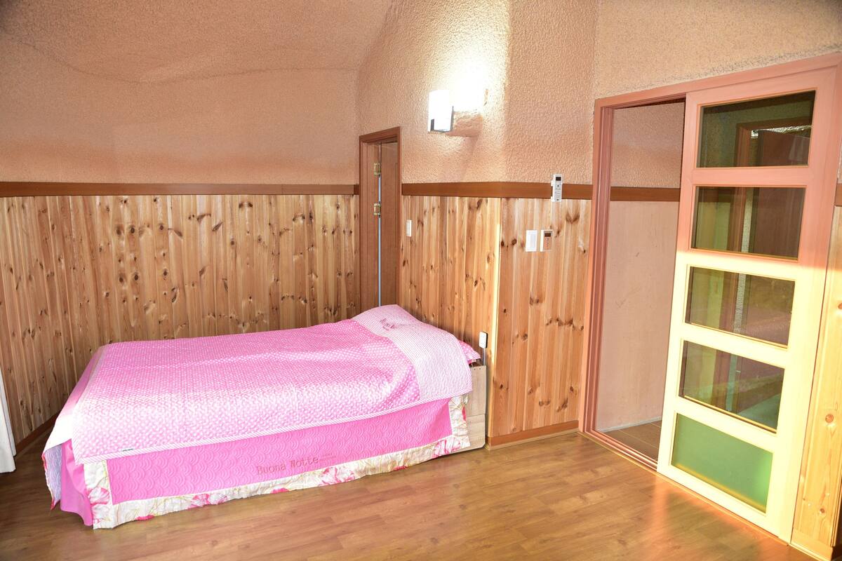 Ein Einzelbett in einem Raum mit Holzwandverkleidung und Holzboden.