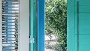A teal door leading to an outdoor area with a view of greenery and a building in the background. - Waterside Paradise! (Thompson Cove)