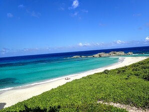 A beach with clear turquoise waters, white sand, and rocky outcrops.