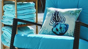 A chair with a blue cushion and a decorative pillow, and a shelf with folded towels. - Waterside Paradise! (Thompson Cove)