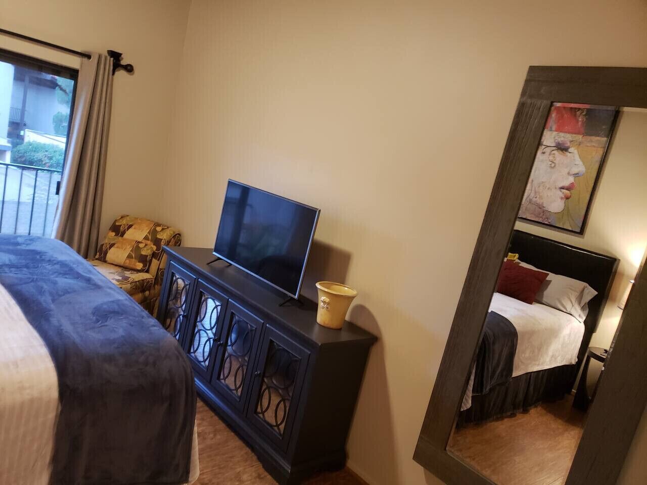 A hotel room with a bed, a TV on a cabinet, a mirror, and a window with curtains.