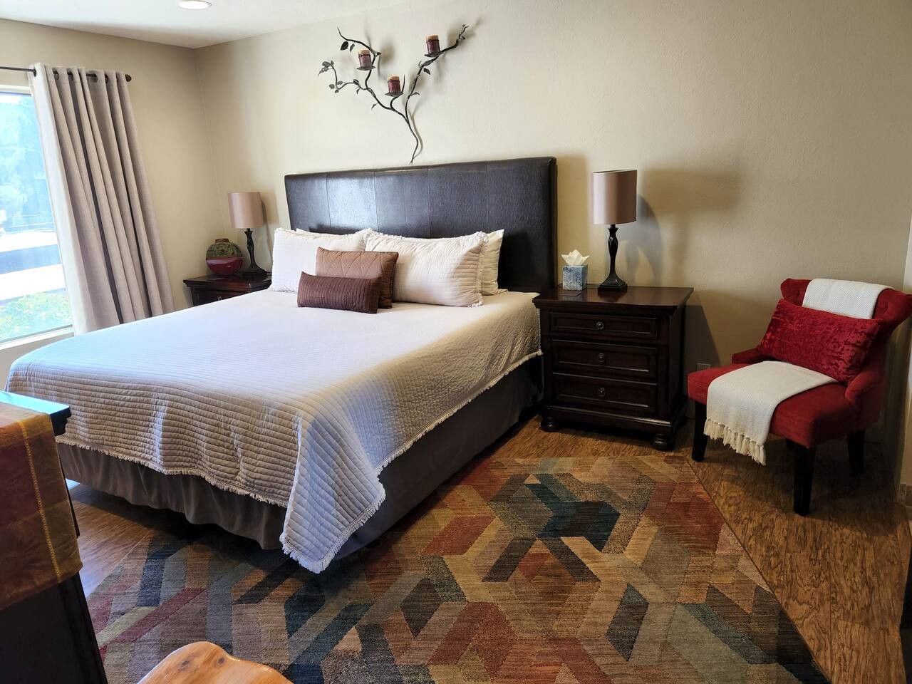 Una habitación de hotel con una cama grande, una mesita de noche, una silla y un adorno en la pared.