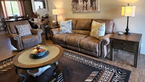 A living room with a brown leather sofa, two armchairs, a coffee table with fruit, a rug, and a painting of horses on the wall. - Johnny's Sedona Getaway - 2 Primary Suites 2 Bath (Sedona)