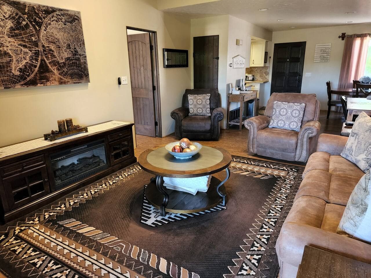 A living room with a round coffee table, two armchairs, a sofa, a fireplace, and a large world map on the wall.