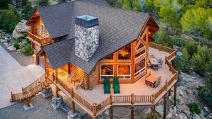 A log cabin with a stone chimney, a deck with outdoor furniture, and a stone foundation. - Jewel of Escalante LLC (Escalante)