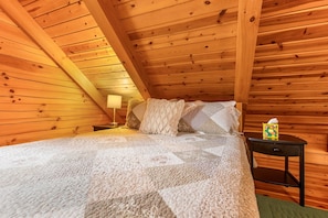 Ein gemütliches Schlafzimmer einer Holzhütte mit Bett, Kissen, Nachttisch und Lampe.