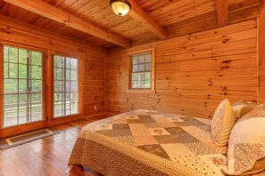 A wooden cabin bedroom with a bed, two windows, and a door.